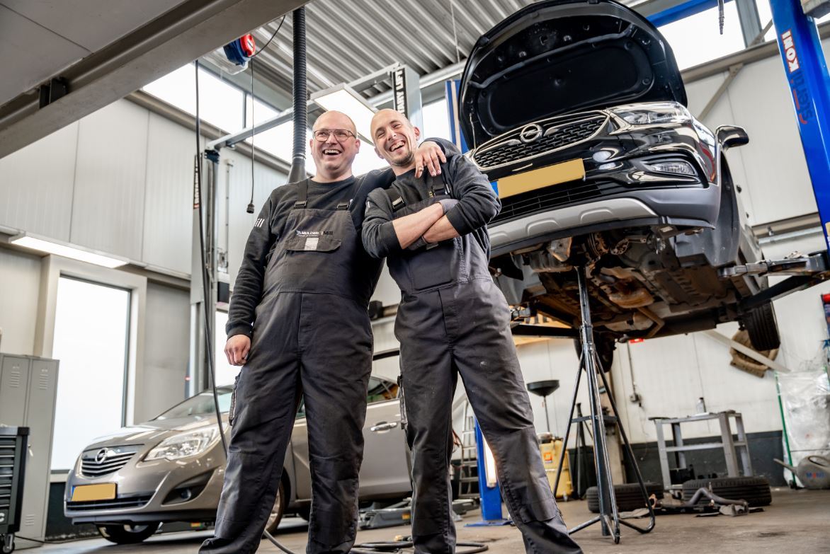 Lachende monteurs met arm over elkaar en auto op de achtergrond