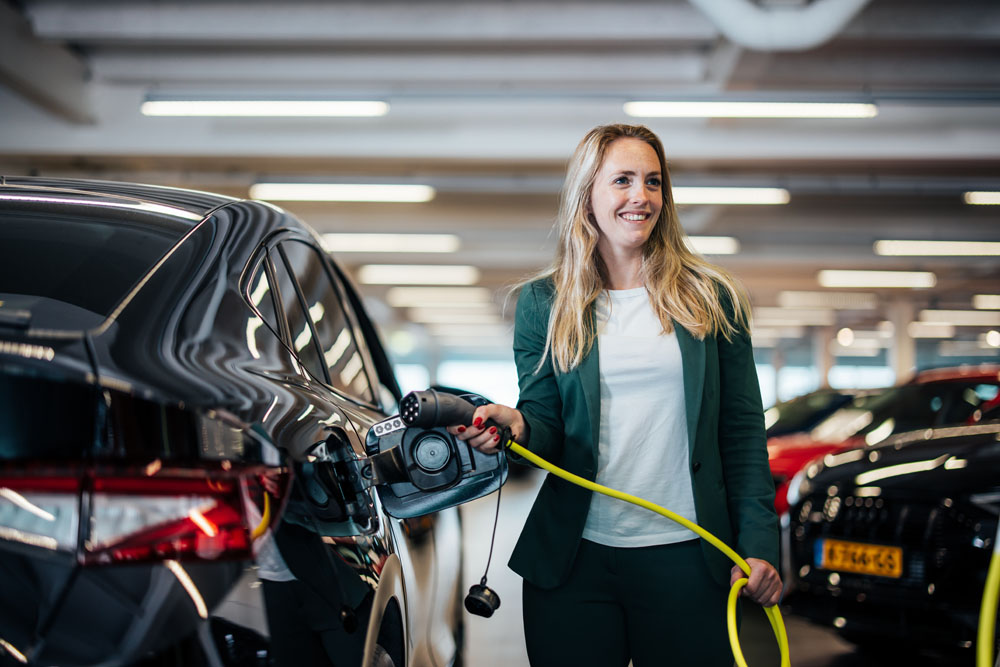 vrouw met een laadkabel die een auto gaat opladen