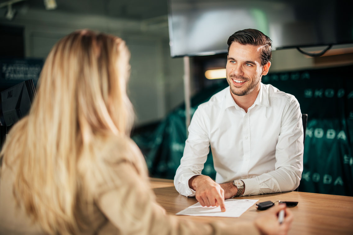 sales medewerker heeft papier voor zich en praat met een klant aan een bureau